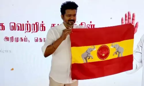 നക്ഷത്രങ്ങളാൽ ചുറ്റപ്പെട്ട വാകപ്പൂവ്, ഇരുവശത്തും ആനകൾ ചുവപ്പും മഞ്ഞയും നിറം നിറഞ്ഞ പാർട്ടി പതാക പുറത്തിറക്കി വിജയ്